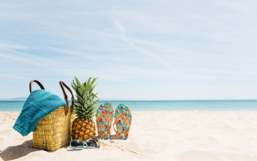 Strand met rieten tas, ananas en slippers aan een blauwe zee. 