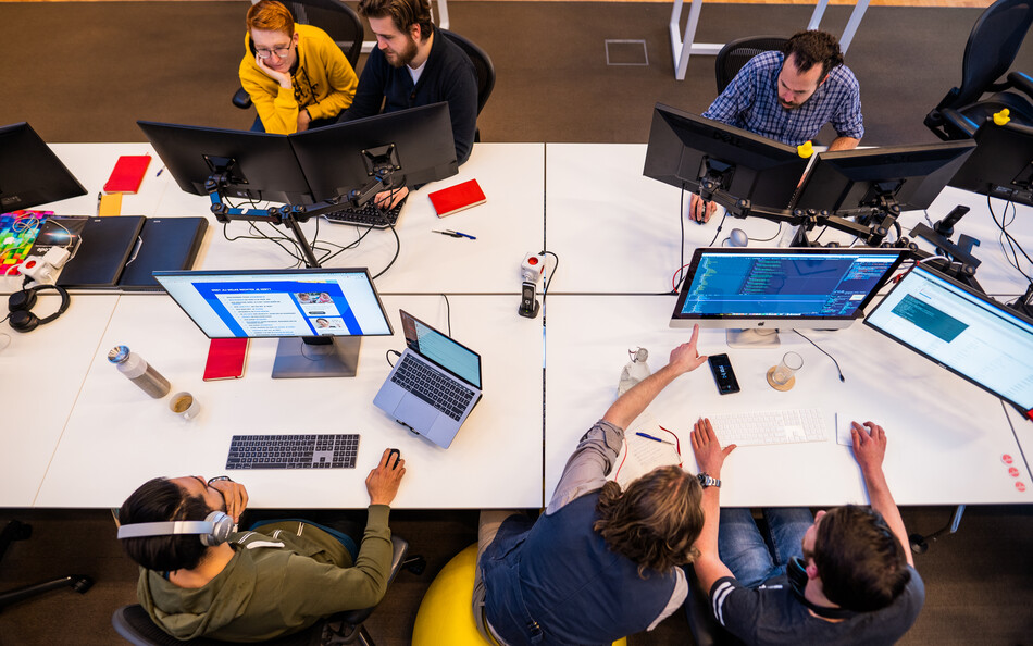 Foto van een bureau-eiland bij SWIS op kantoor waaraan developers aan het werk zijn