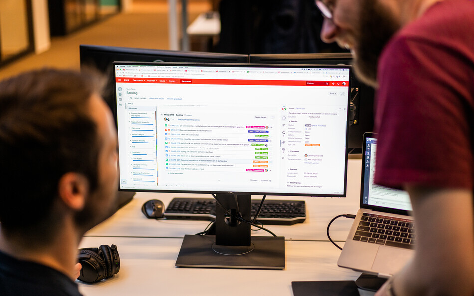 Twee SWIS collega's kijk naar een monitor met daarop een backlog