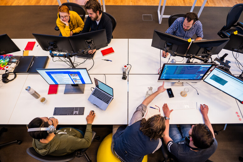 Foto van een bureau-eiland bij SWIS op kantoor waaraan developers aan het werk zijn